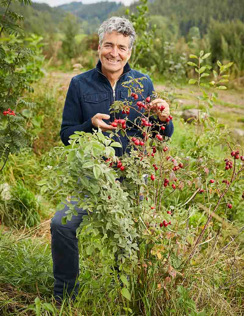 Lächelnder Mann mit grauem Haar an einem Strauch mit roten Früchten am Feldrand