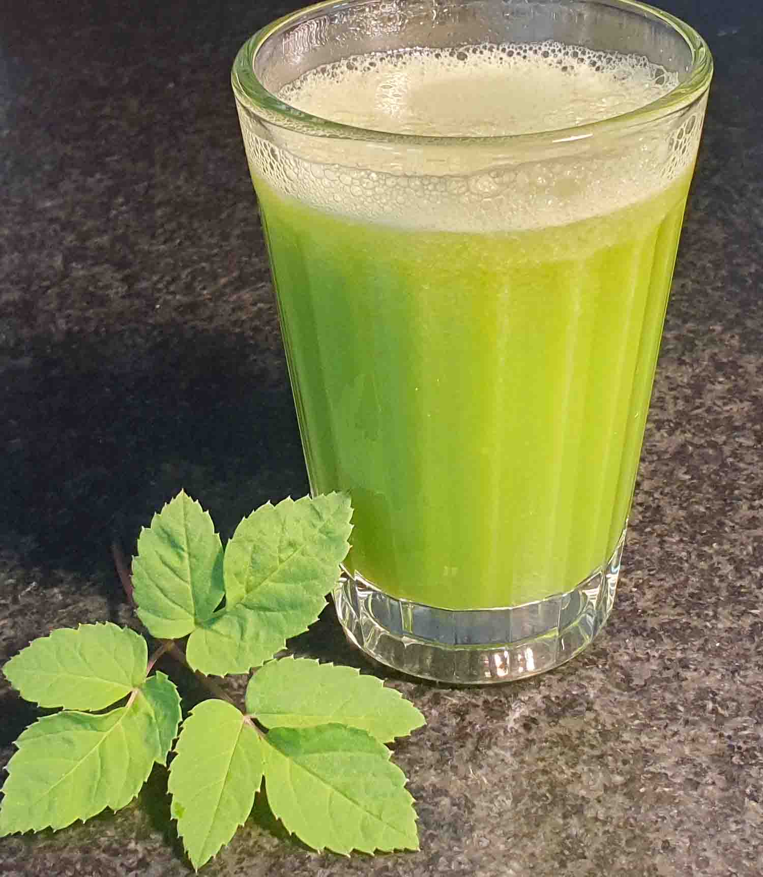 Glas mit hellgrünem Saft auf dunkler Arbeitsplatte, daneben ein gezähntes grünes Blatt