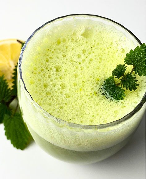 Hellgrüner Brennnessel-Smoothie im Glas, garniert mit einem Blatt, daneben eine Zitrone