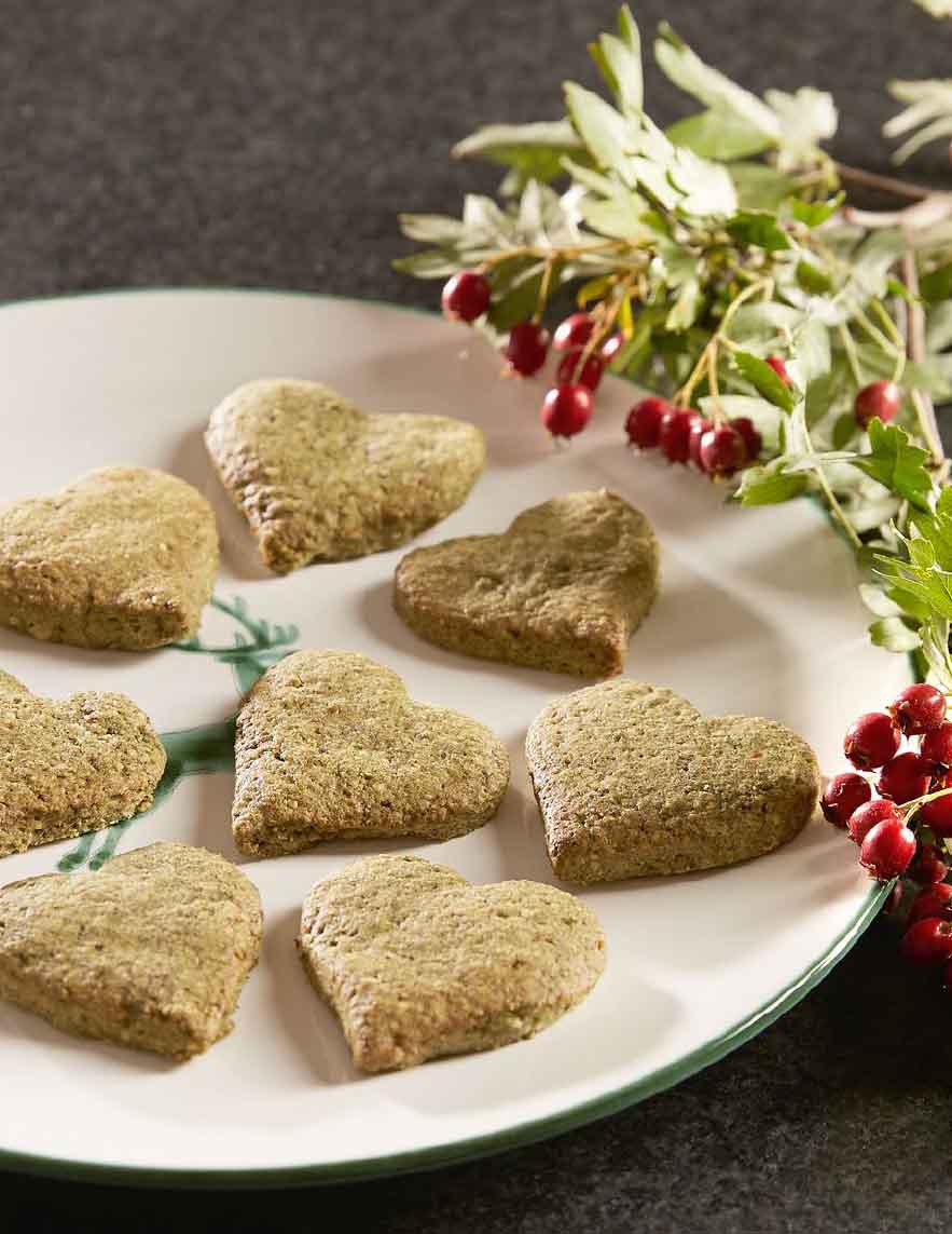 Herzförmige grünliche Kekse auf einem weißen Teller, daneben ein Zweig mit roten Beeren