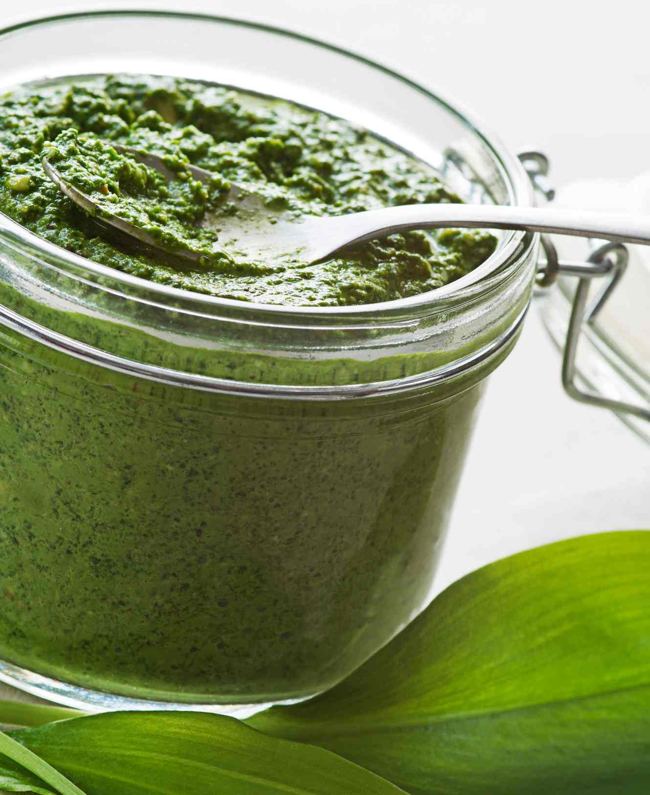 Bärlauchpesto im Bügelglas mit Löffel, daneben frische Bärlauchblätter