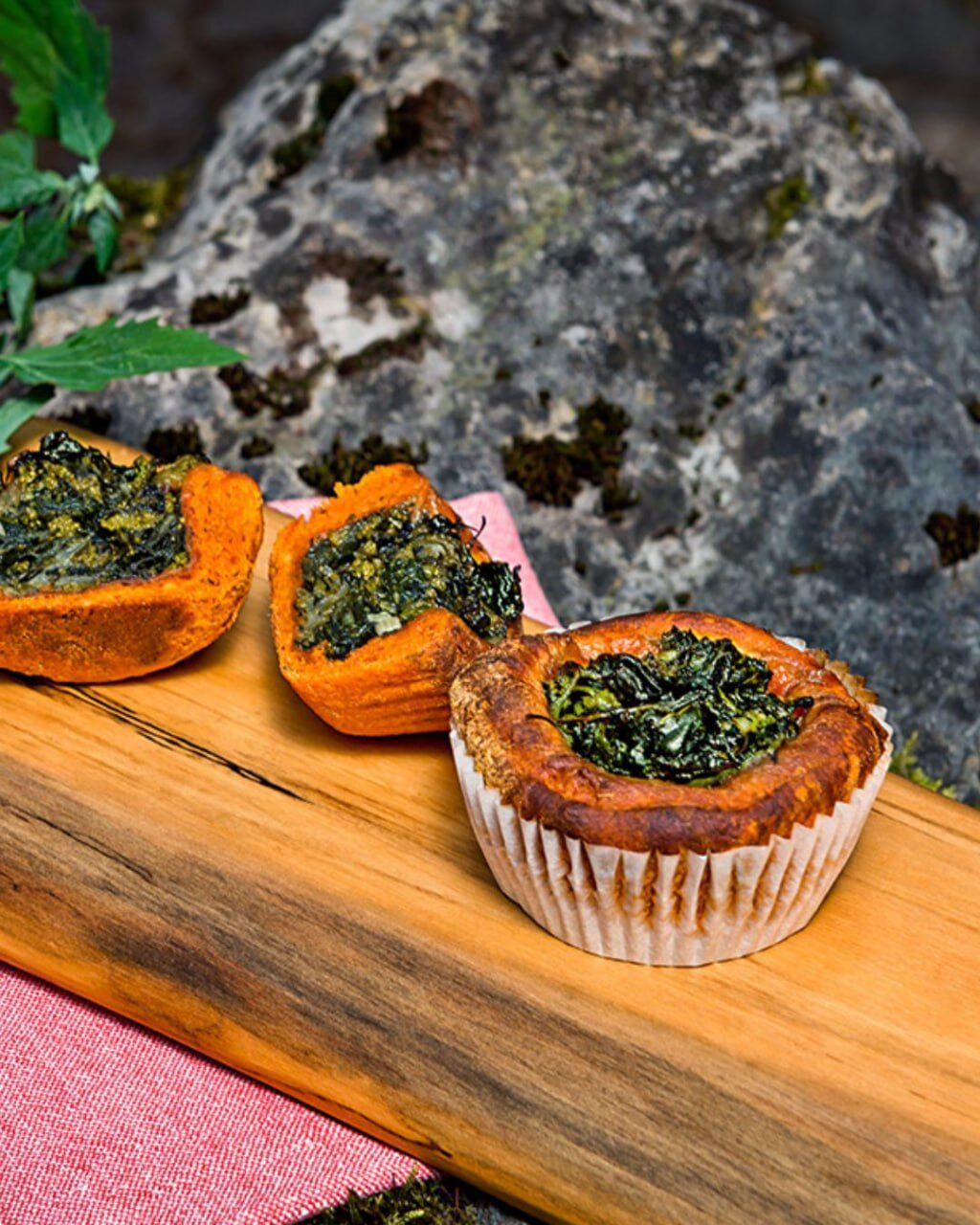 Drei herzhafte Muffins mit dunkelgrüner Kräuterfüllung auf einem Holzbrett vor einem Felsen