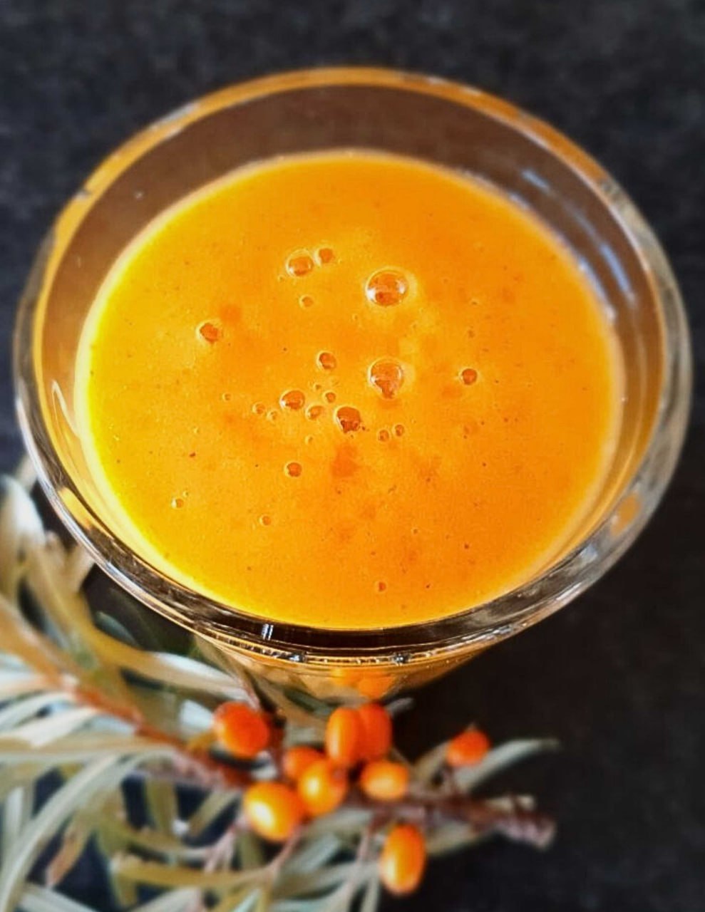 Sanddorn-Smoothie in einem Glas, davor ein Sanddornzweig mit Beeren
