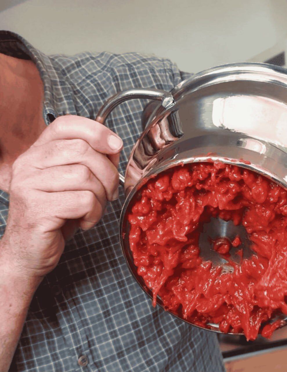 Ein Mann im karierten Hemd hält eine Passiermühle mit leuchtend rotem Fruchtmus