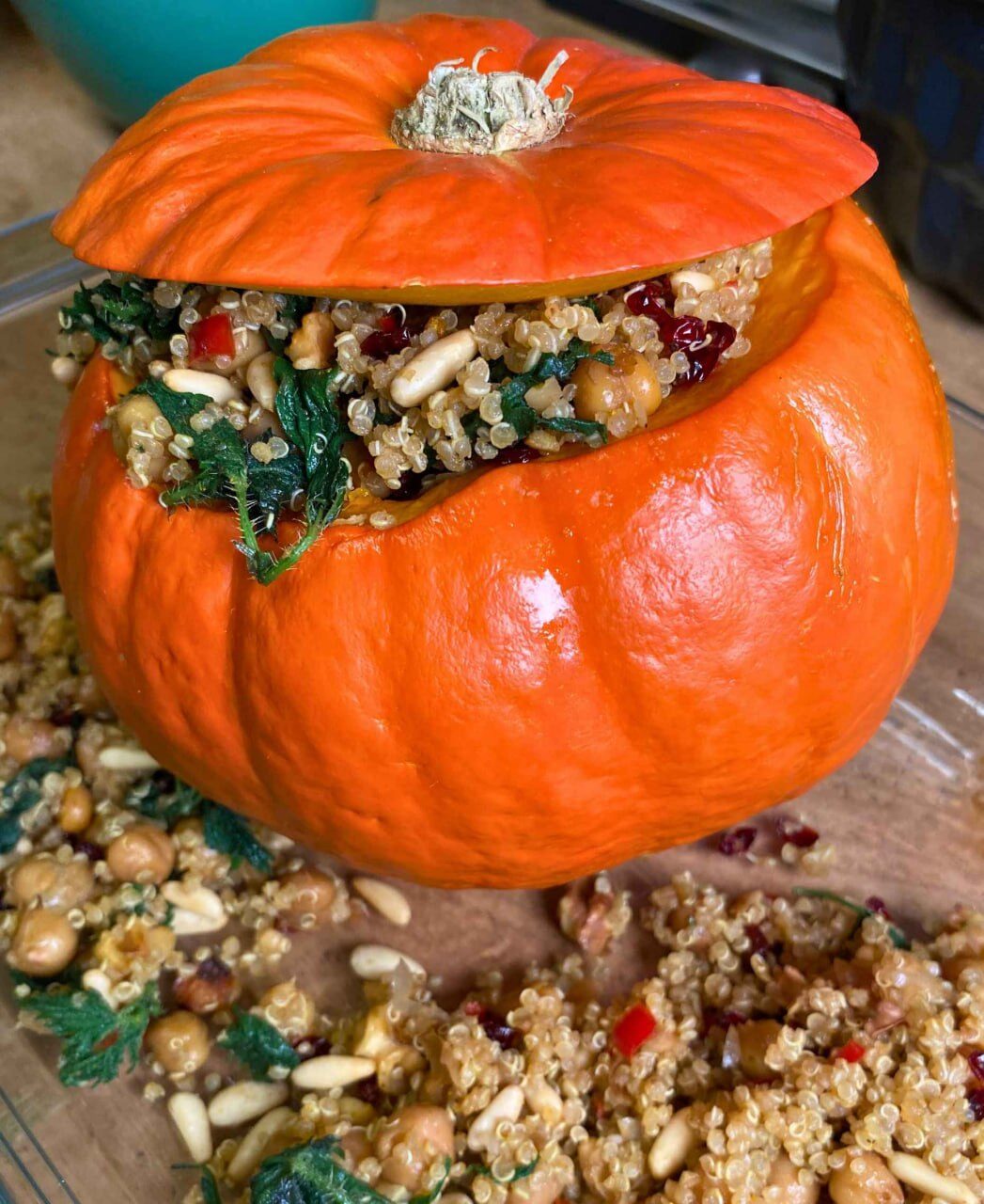 Ausgehöhlter oranger Kürbis mit Deckel, gefüllt mit Quinoa, Kichererbsen, Pinienkernen und Wildkräutern