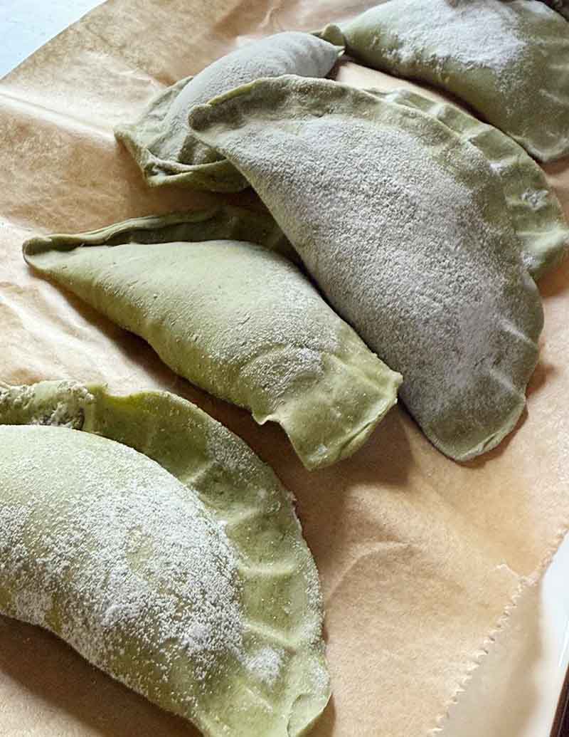 Ungekochte grünliche Teigtaschen, mit Mehl bestäubt, auf Backpapier